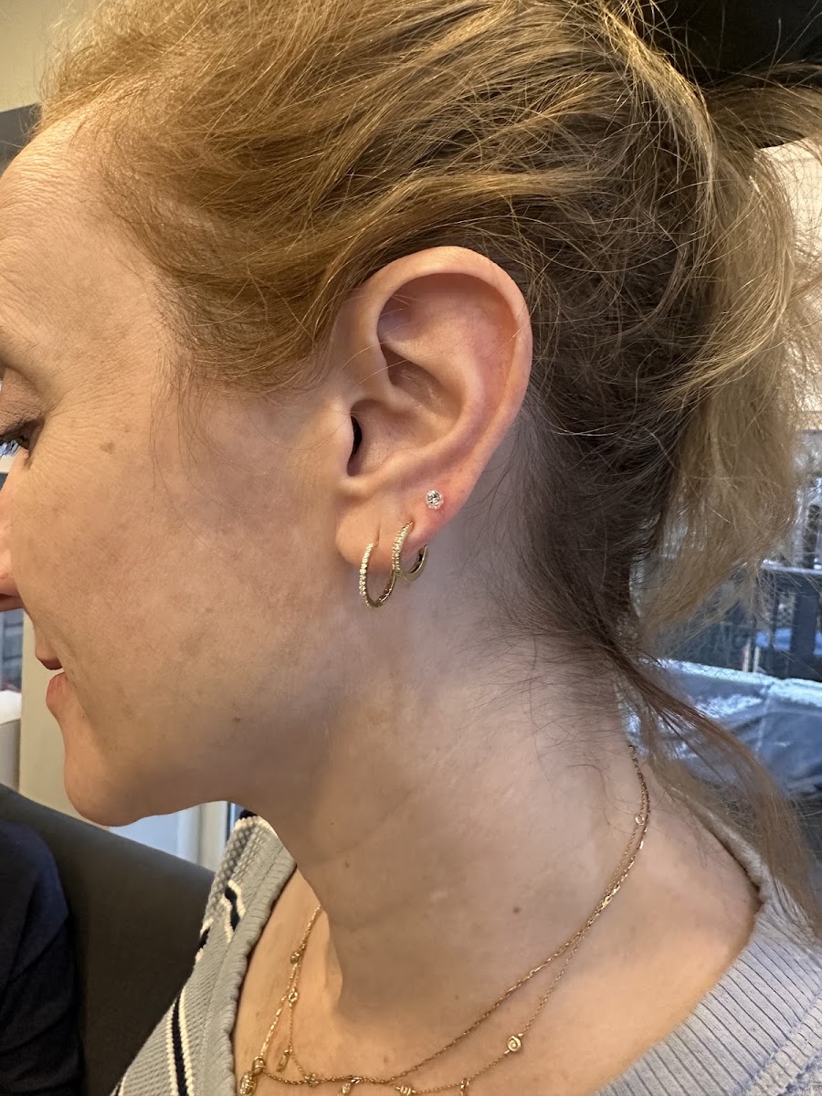 Side view of an ear with small hoop and stud earrings